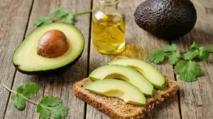 Avocado a metà e fette su pane integrale con bottiglietta di olio e prezzemolo su tavolo di legno