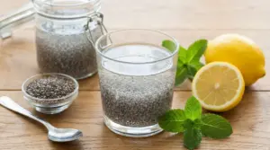 Bicchiere di acqua di chia con semi di chia, limone e foglie di menta su un tavolo di legno