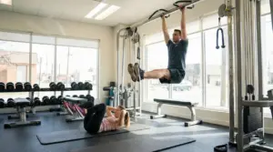 Persona che esegue leg raises alla sbarra e persona che fa crunch su tappetino in palestra