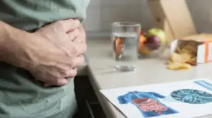 Persona con le mani sull’addome, con bicchiere d’acqua e schema dell’apparato digerente sul tavolo