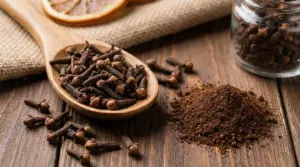 Chiodi di garofano interi in un cucchiaio di legno e polvere di chiodi di garofano su un tavolo rustico