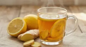 Tisana calda zenzero e limone in tazza di vetro con fettine di limone e zenzero su tavolo di legno